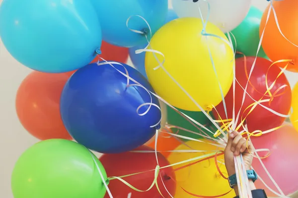 A hand holding a bunch of bright party balloons