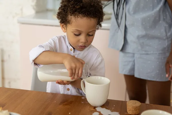 A small child carefully pouring milk from a little bottle into a cup at the kitchen table