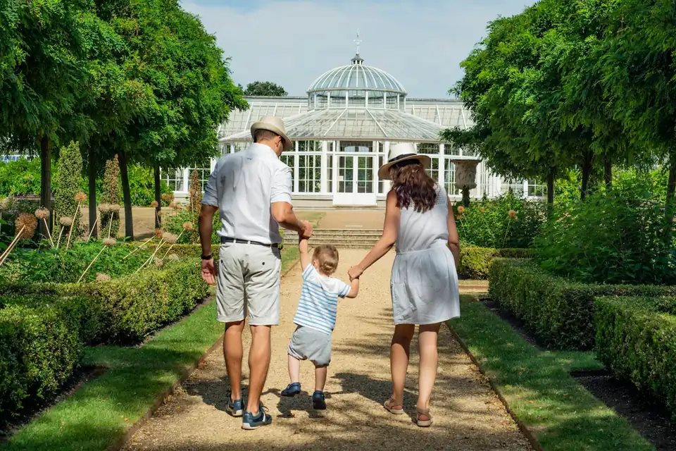A parent couple and their small child walking hand in hand down a garden path, seen from behind