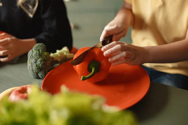 Two children's hands cutting a red pepper on a plate
