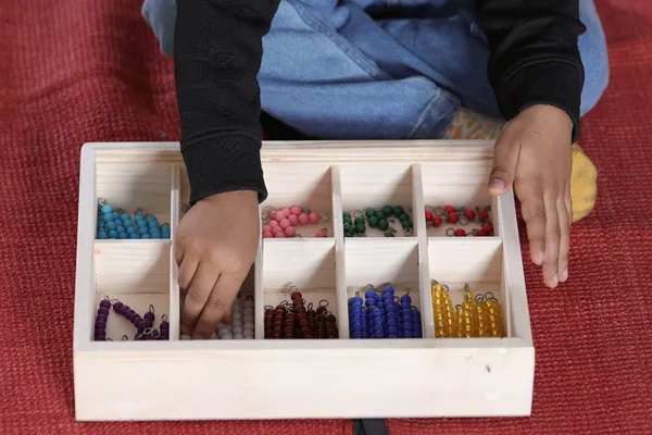 A child's hands sorting colored beads in a wooden box