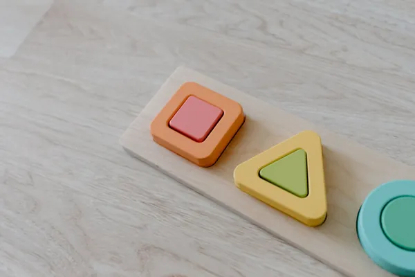 A wooden shape-sorting puzzle with square, triangle and circle pieces