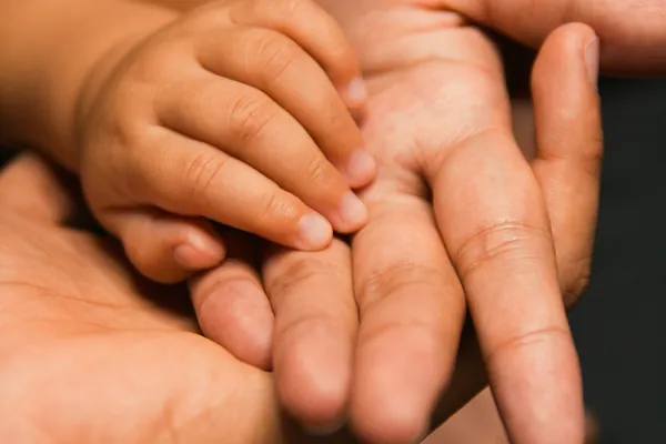 A parent's hand holding a baby's small hand