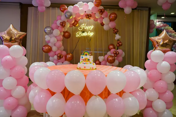 A birthday party table with cake and pink and white balloons