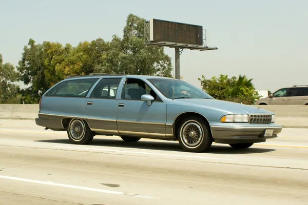 A light blue station wagon driving down a highway on a sunny day